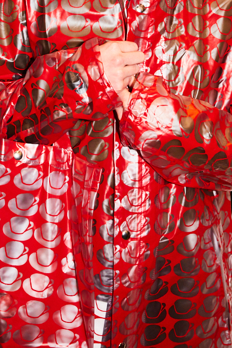 Roter, glänzender Mantel mit asymmetrischem Design aus kreisförmigen Mustern, eng um die Person gewickelt.