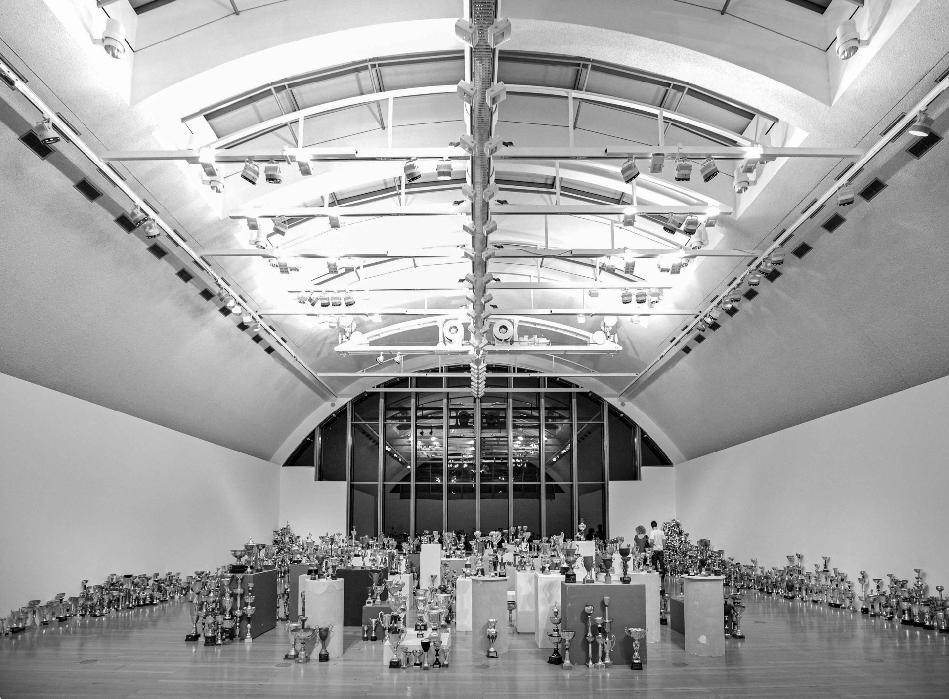 Ausstellungshalle mit zahlreichen Trophäen, beleuchtet von modernen Deckenleuchten, in Schwarz-Weiß.