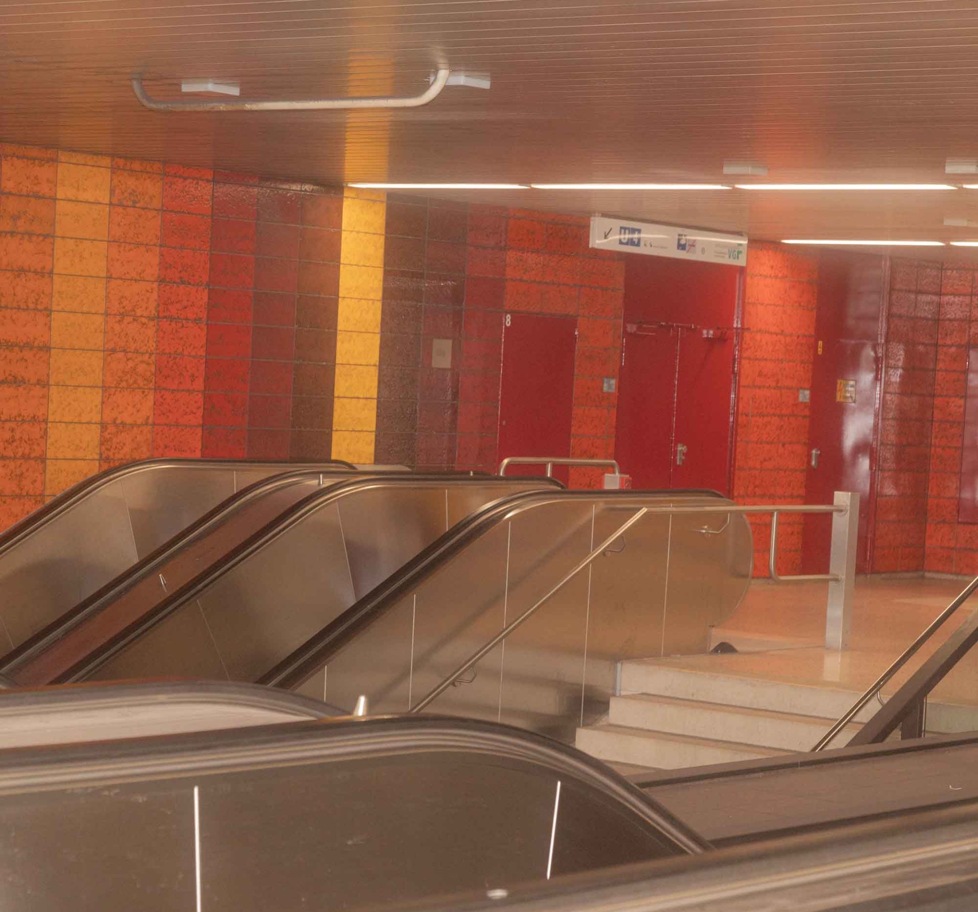 Leere U-Bahn-Station mit rollenden Treppen und bunten Wänden in Rot- und Gelbtönen.