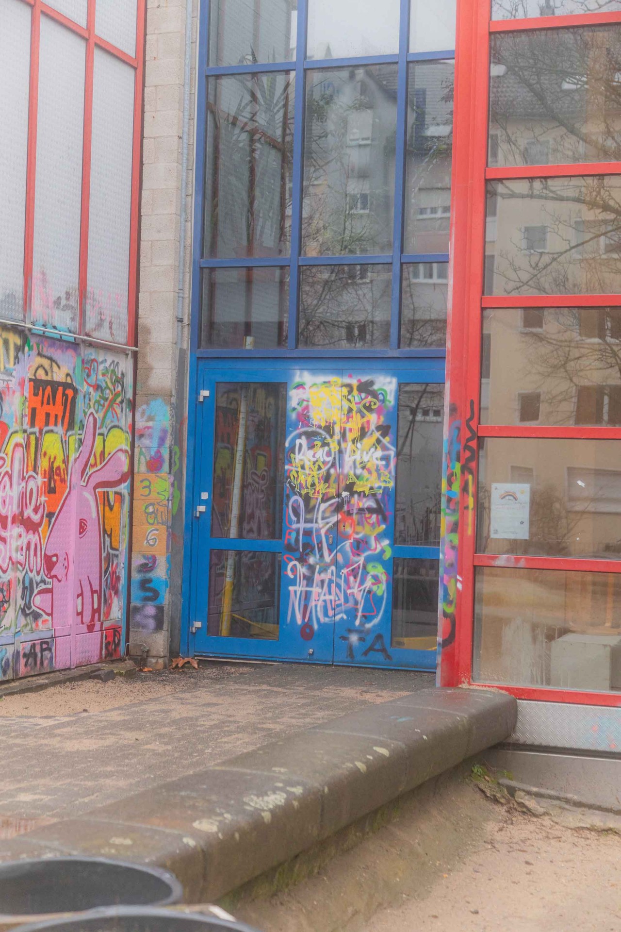 Bunte Graffitis und eine blaue Tür an einem modernen Gebäude, umgeben von urbanen Elementen.