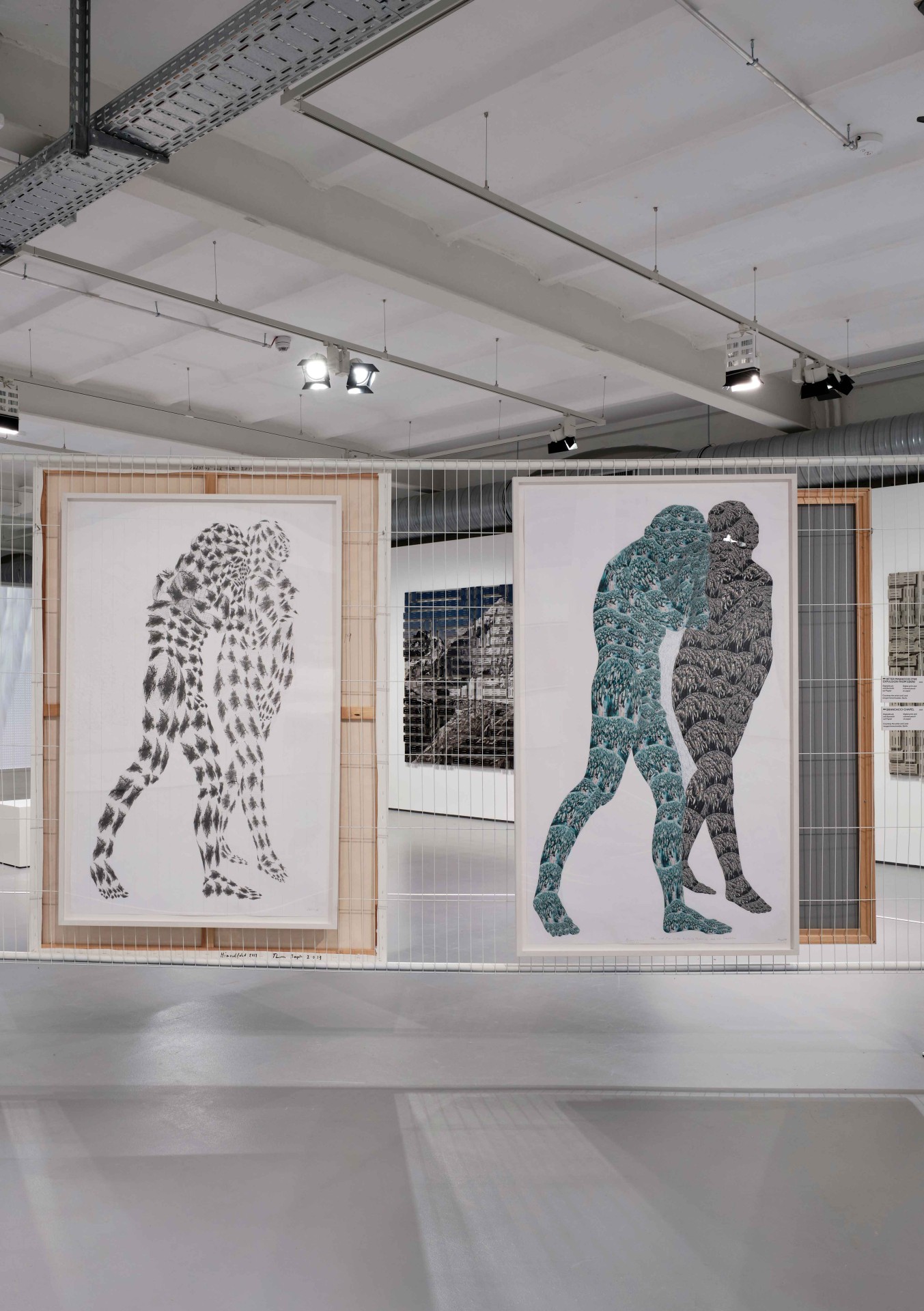 Zwei große Kunstwerke in einem Ausstellungsraum mit stilisierten, umarmenden Figuren. Minimalistische Umgebung.