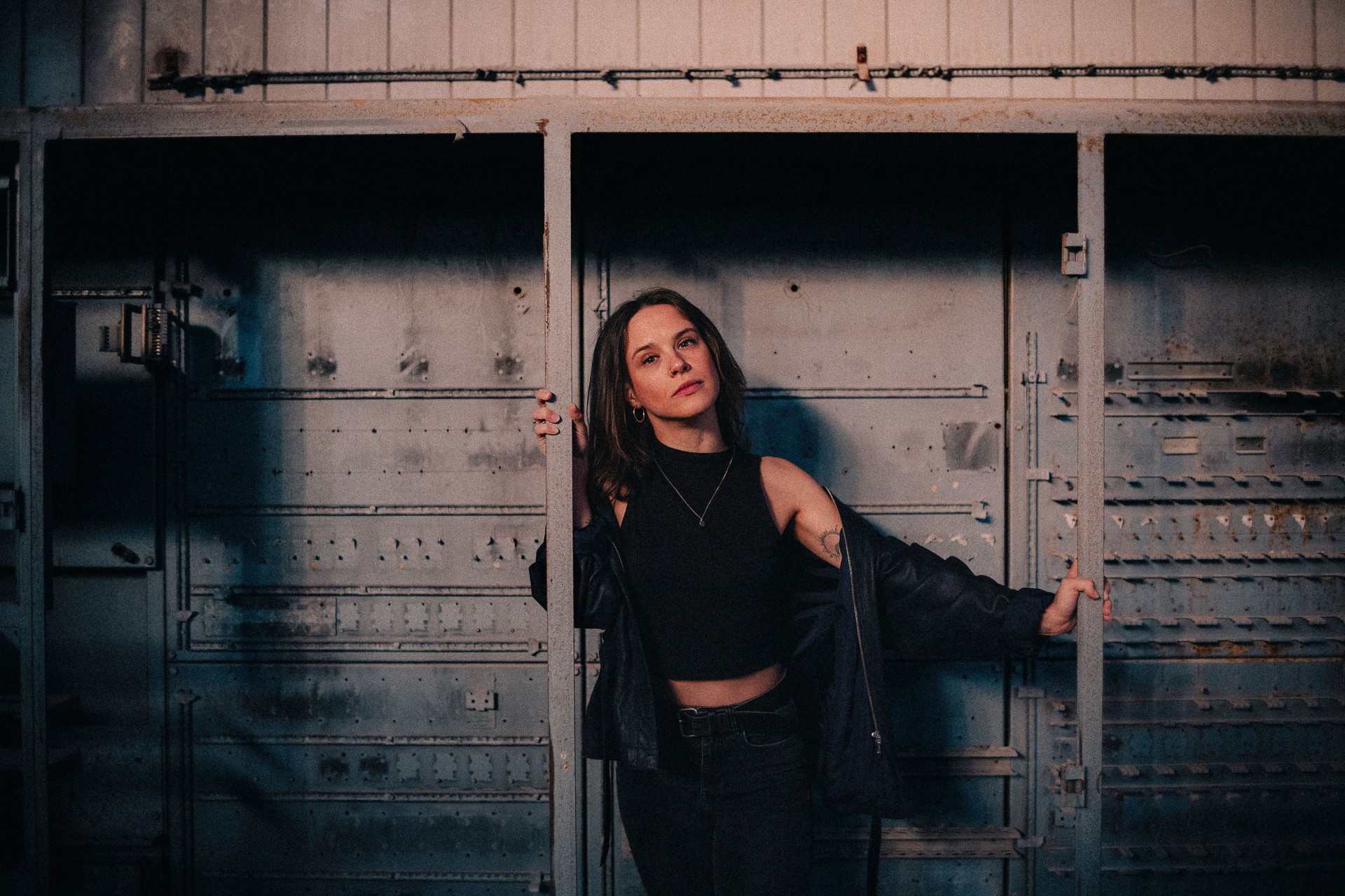 Frau in dunklem Top steht in metallischer Umgebung und blickt direkt in die Kamera.