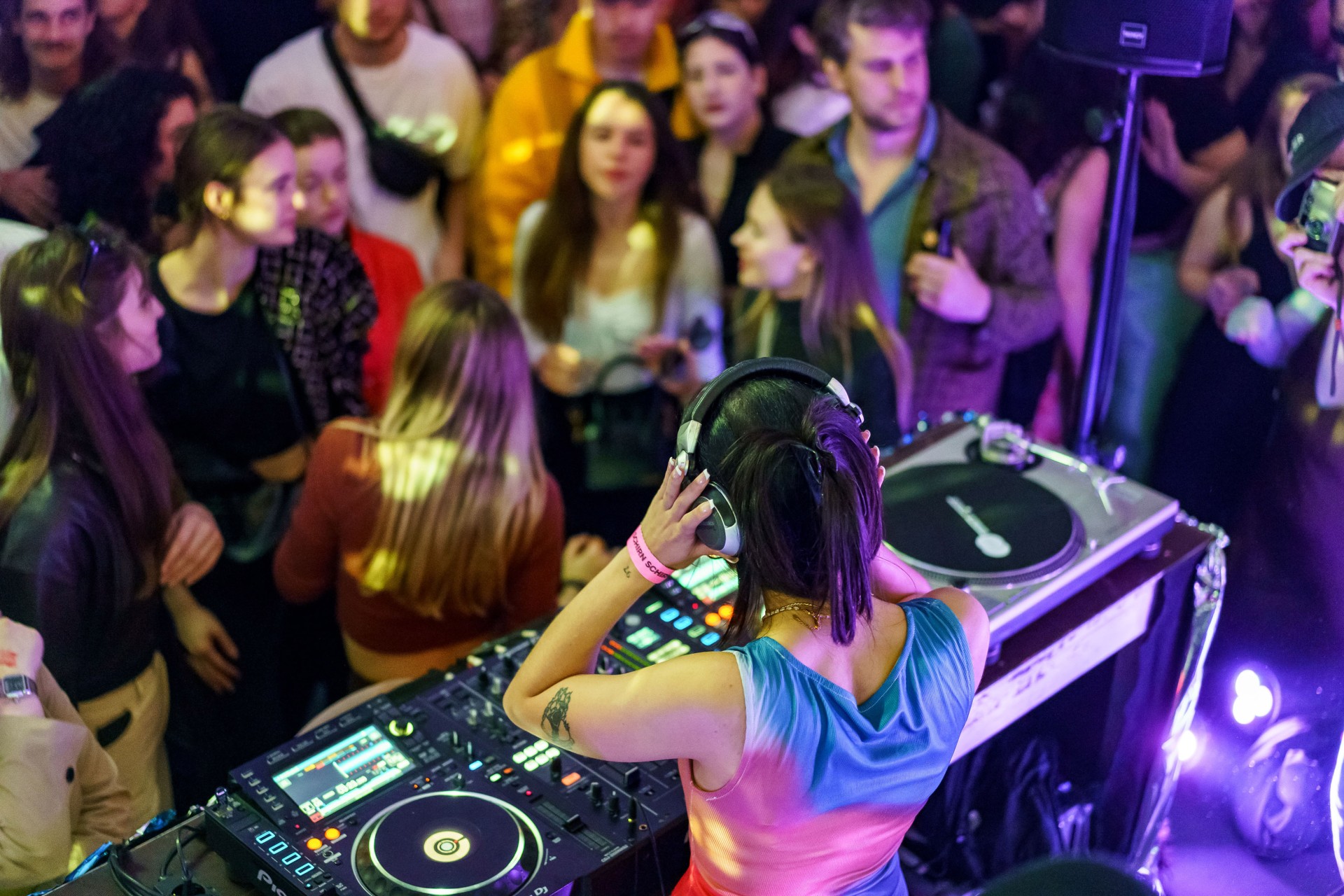 DJ legt in einer coolen Location mit buntem Licht vor einer Menge Musik auf.