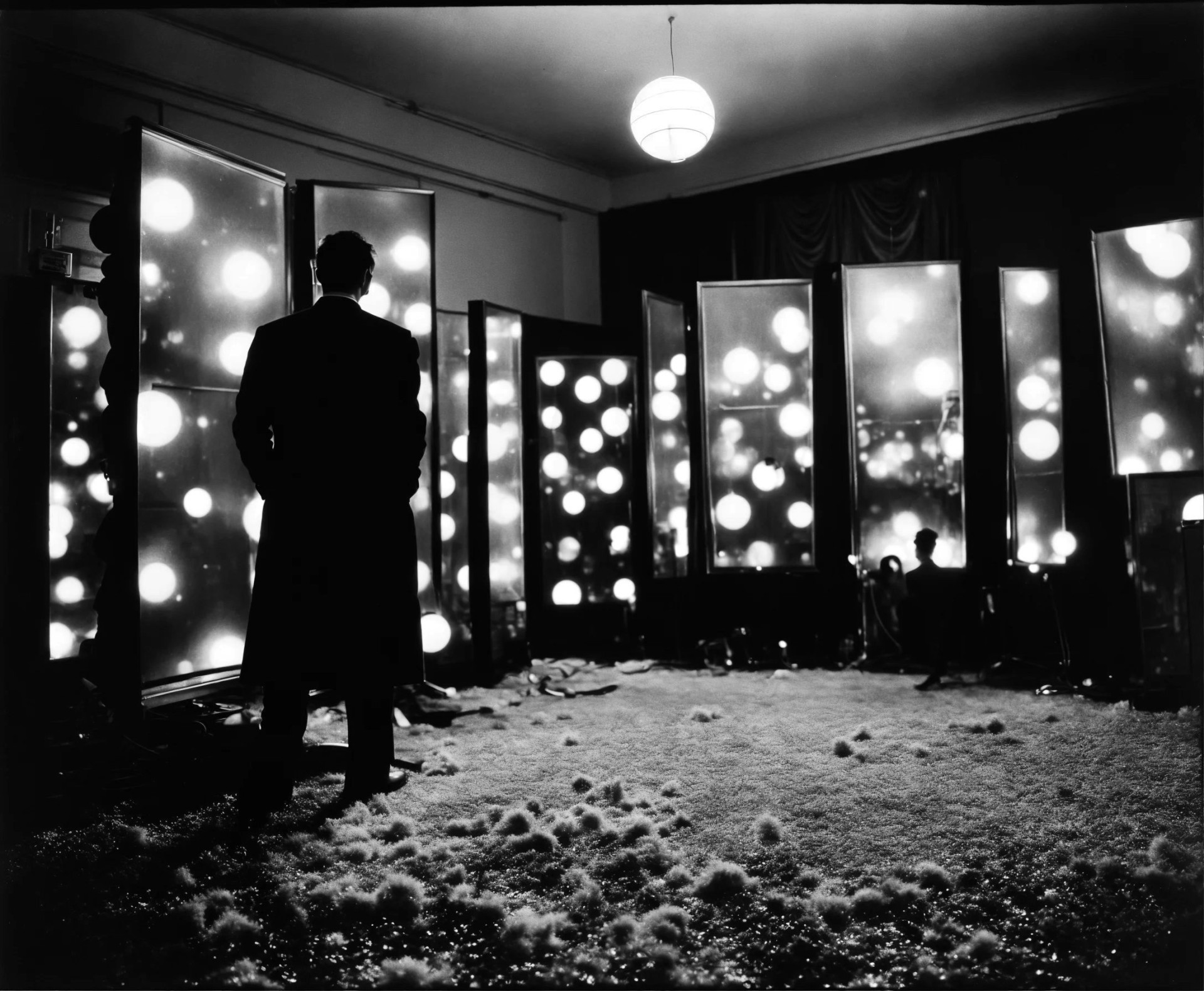 A man in a room looks at illuminated backgrounds with blurred light spots and a messy floor.