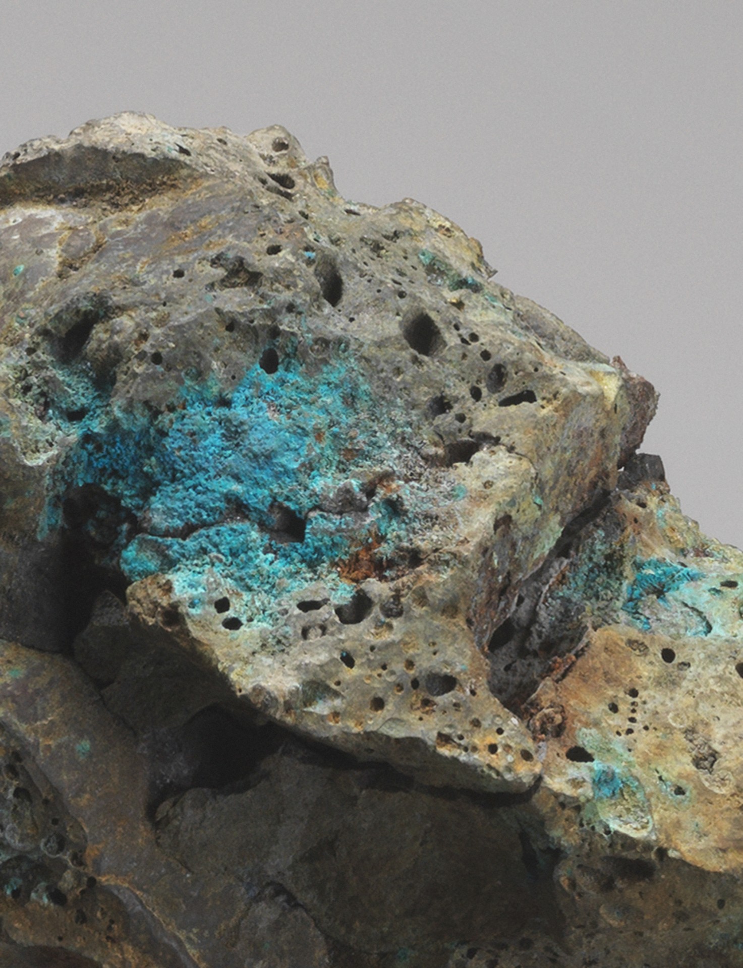 Close-up of a mineral rock featuring green and blue hues with many small holes and uneven surfaces.