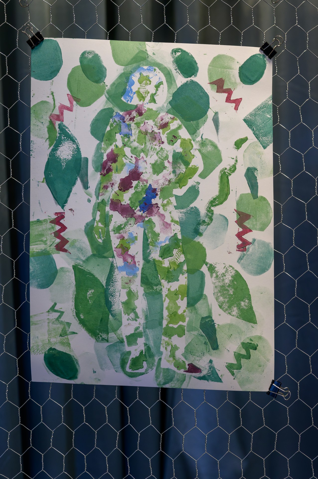 Kreative Farbdruckgrafik einer Figur umgeben von grünen Blättern und abstrakten Formen auf weißem Hintergrund.
