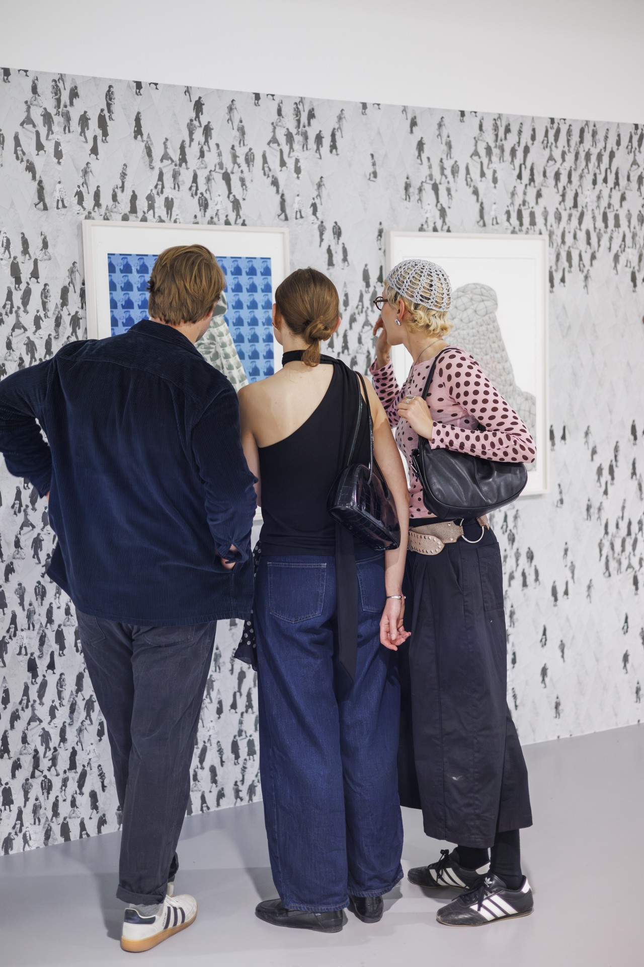 Drei Personen bewundern Kunstwerke in einer Galerie mit einem grafischen Hintergrund.