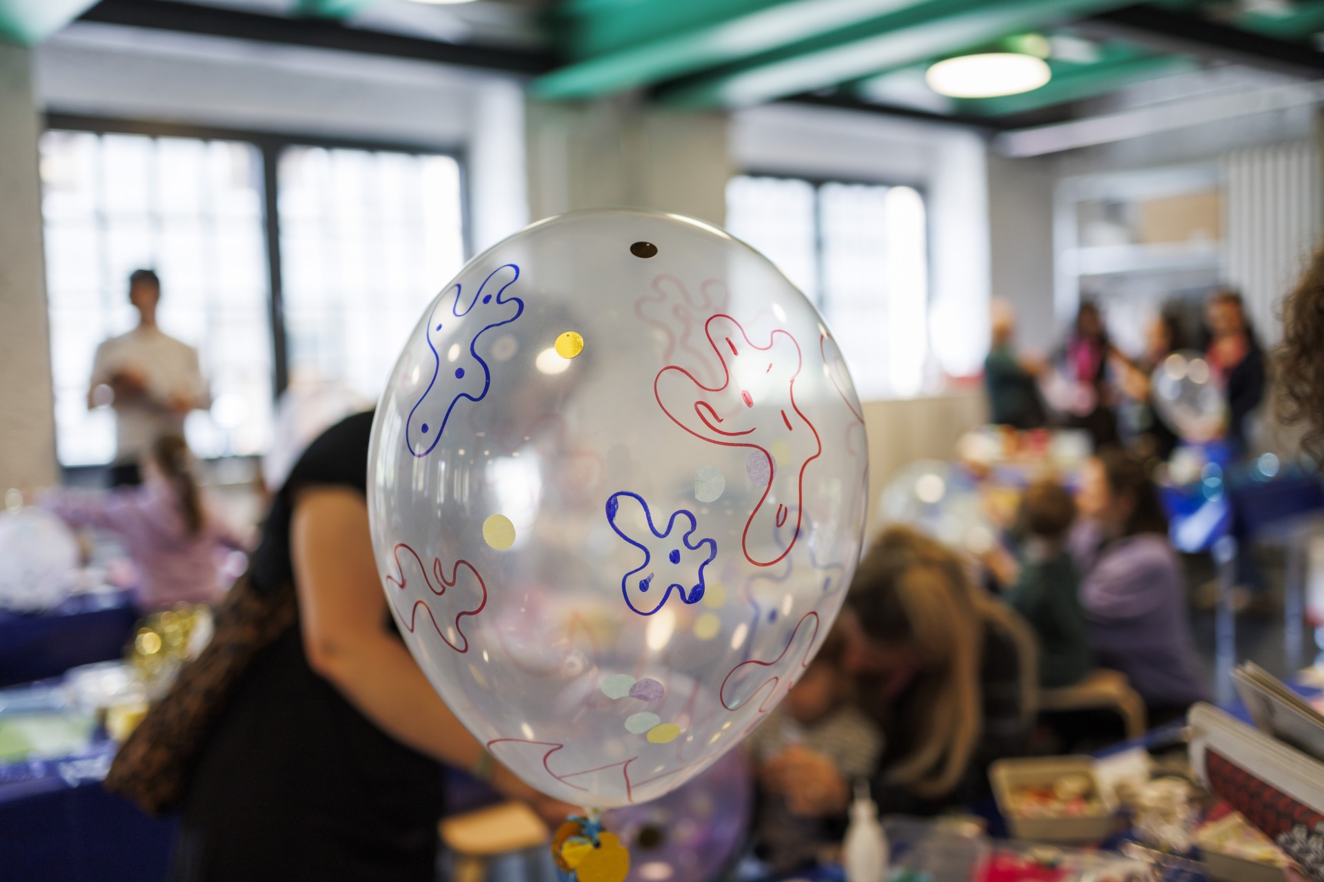 Ein bunter Luftballon mit farbenfrohen Mustern im Vordergrund, während Menschen im Hintergrund aktiv sind.