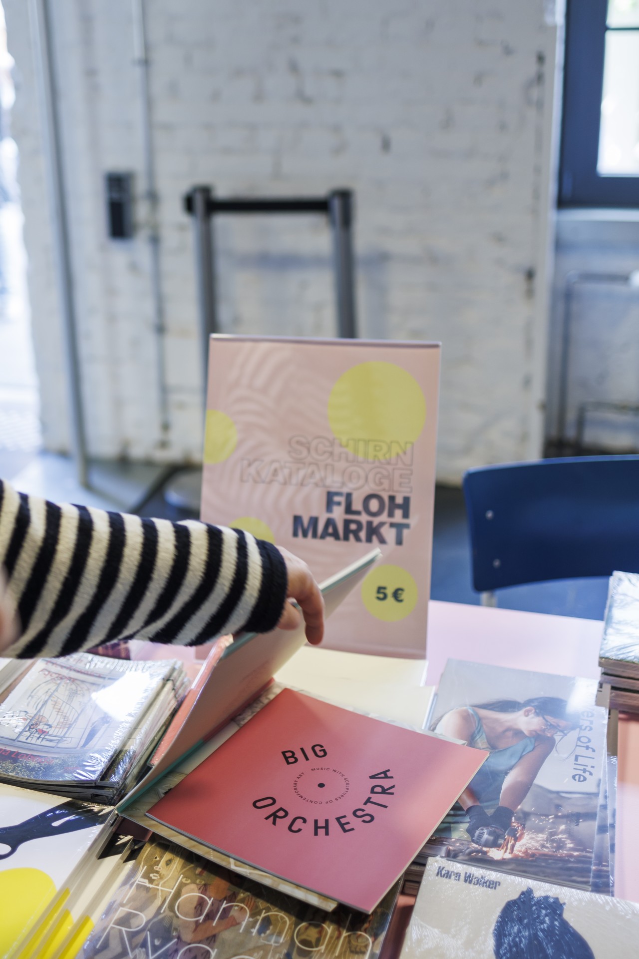 Flohmarkt mit Katalogen und Büchern, darunter "BIG ORCHESTRA", auf einem Tisch mit Preisschild.