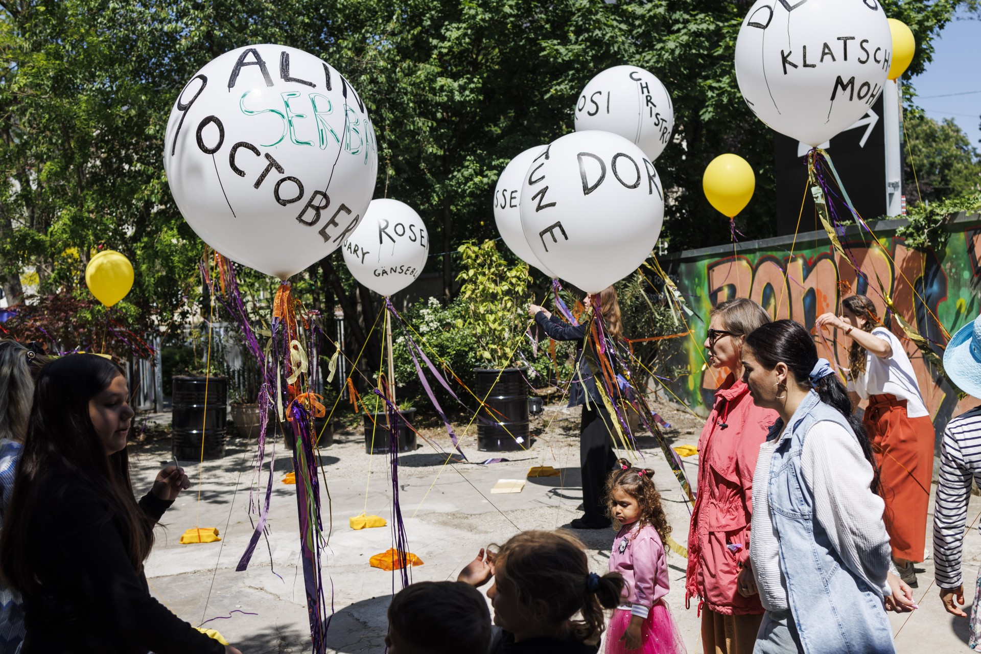 Menschen feiern mit luftgefüllten Ballons, die mit bunten Bändern in einer lebhaften, grünen Umgebung geschmückt sind.