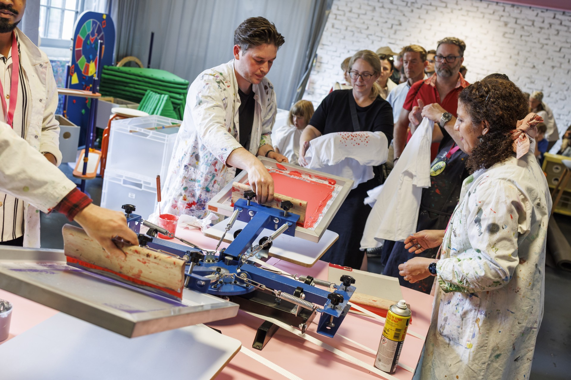 Menschen in einem Textildruck-Workshop drucken bunte Motive auf T-Shirts.