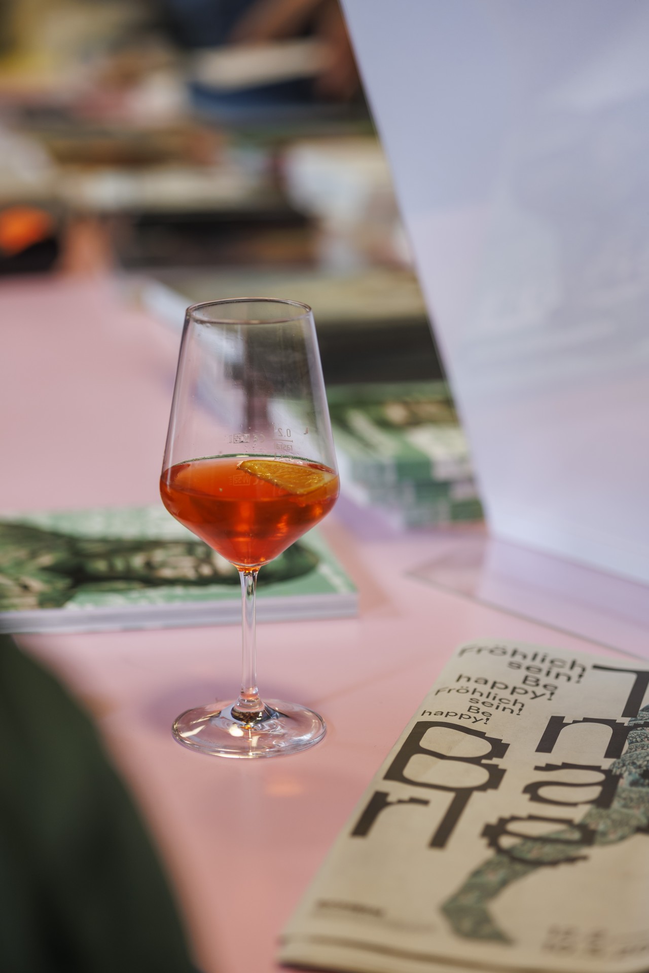 Ein Glas mit orangefarbenem Getränk steht auf einem pinken Tisch, umgeben von Zeitschriften.