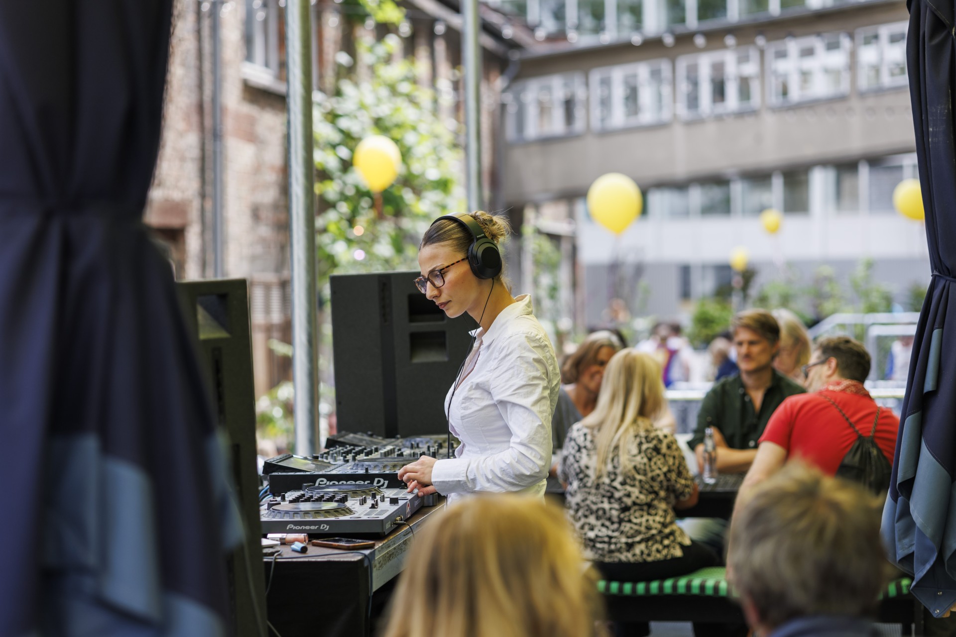 DJ bei einer Open-Air-Veranstaltung, umgeben von Menschen und bunten Luftballons, sorgt für musikalische Unterhaltung.