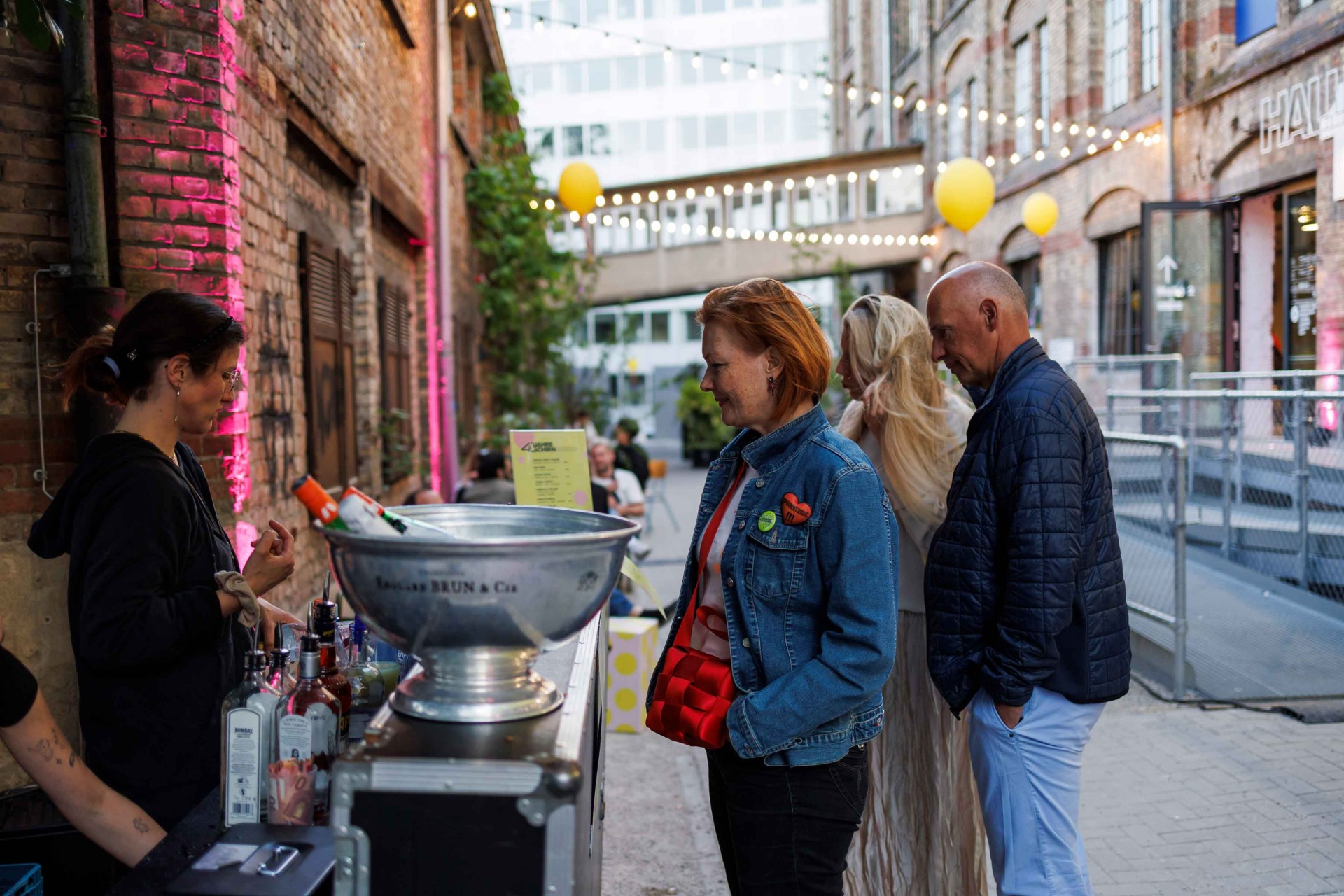 Colorful atmosphere in an urban alley with guests at a bar stand and festive decorations.