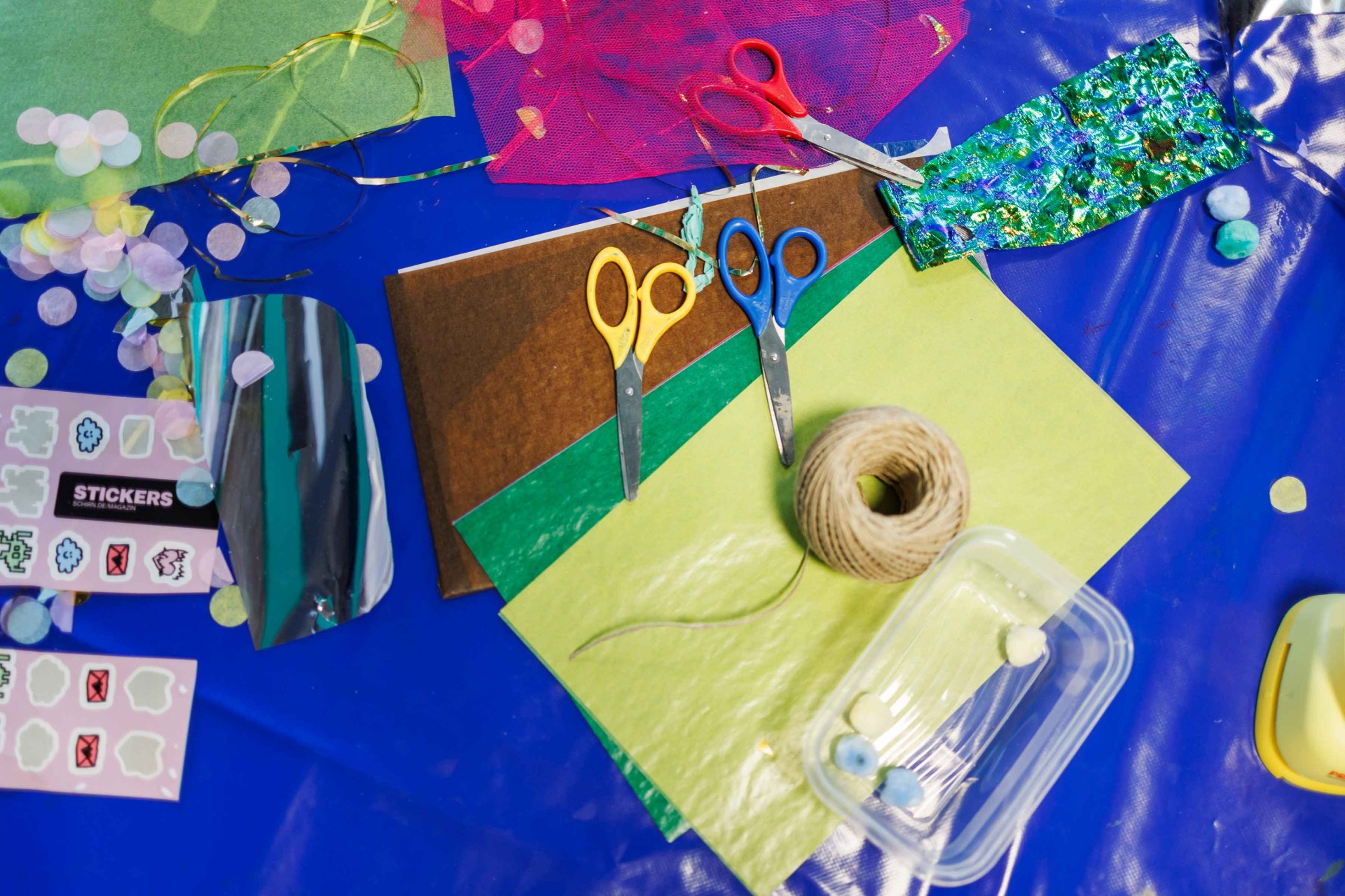 Craft materials like paper, scissors, string, and stickers on a blue table.
