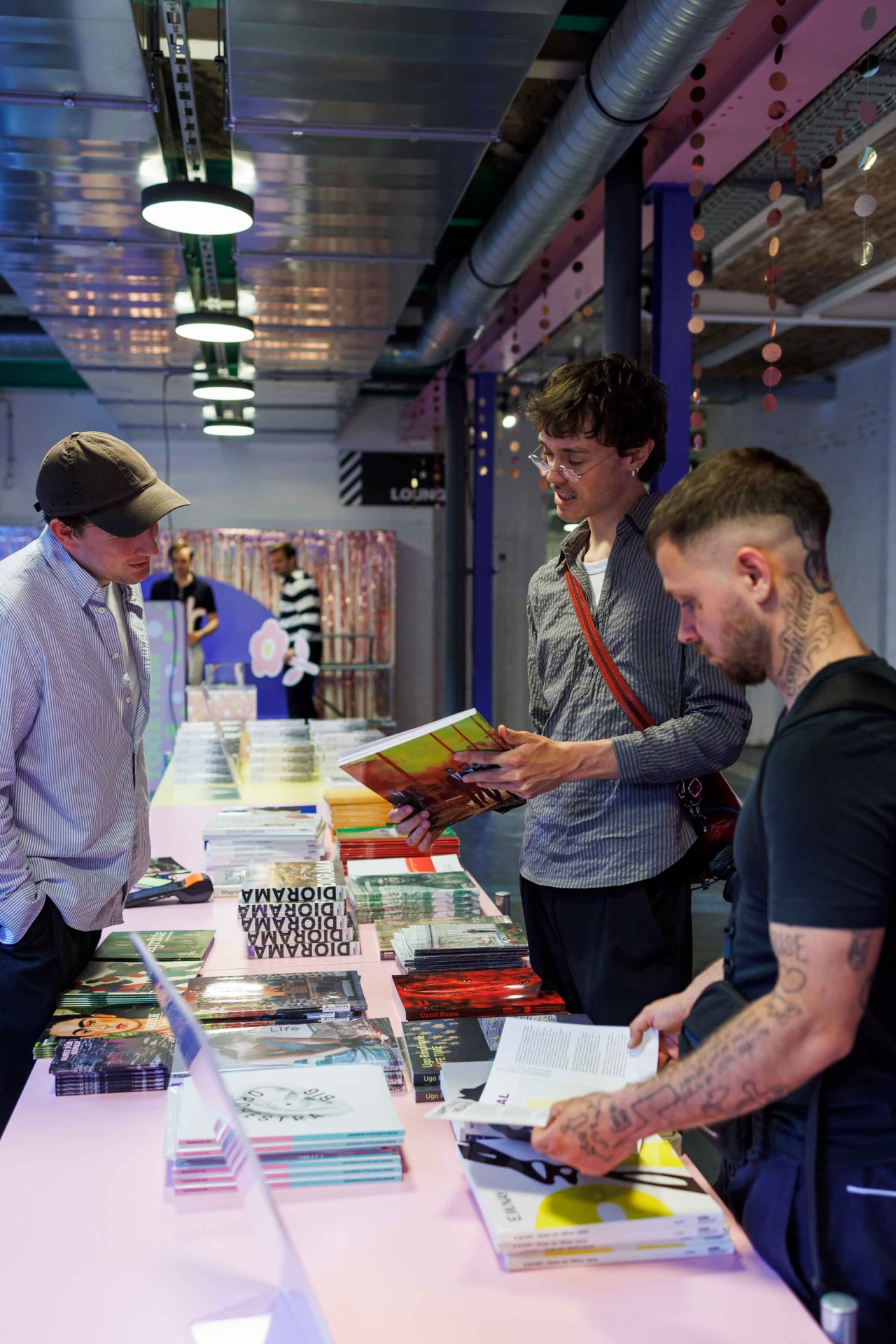 Three men are looking at books on a colorful table in a modern room, surrounded by creative decorations.
