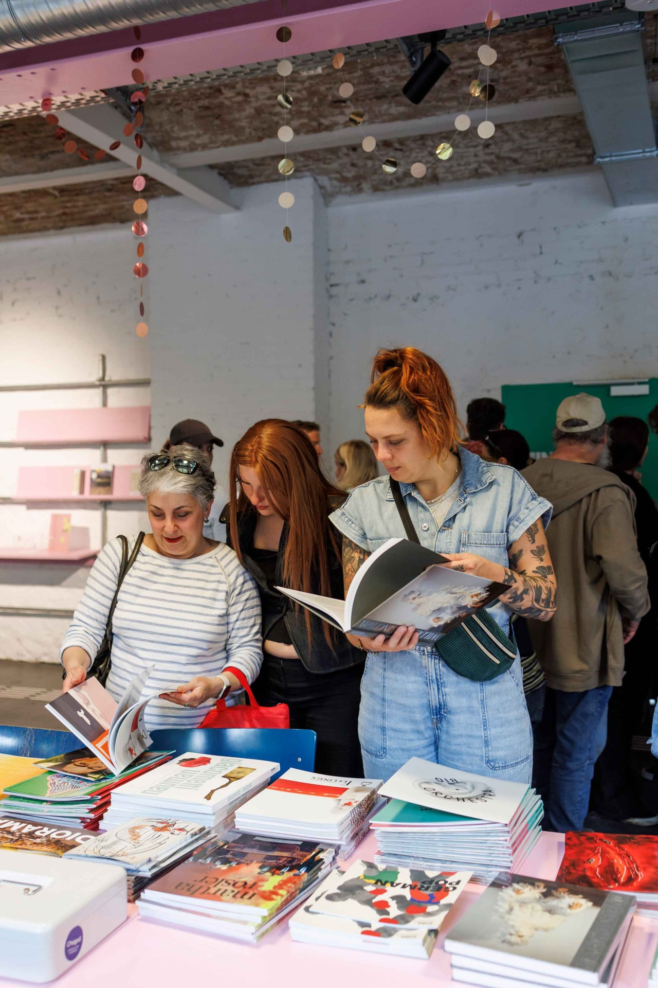 Three people are looking at books at a table in a bright room with decorative elements.