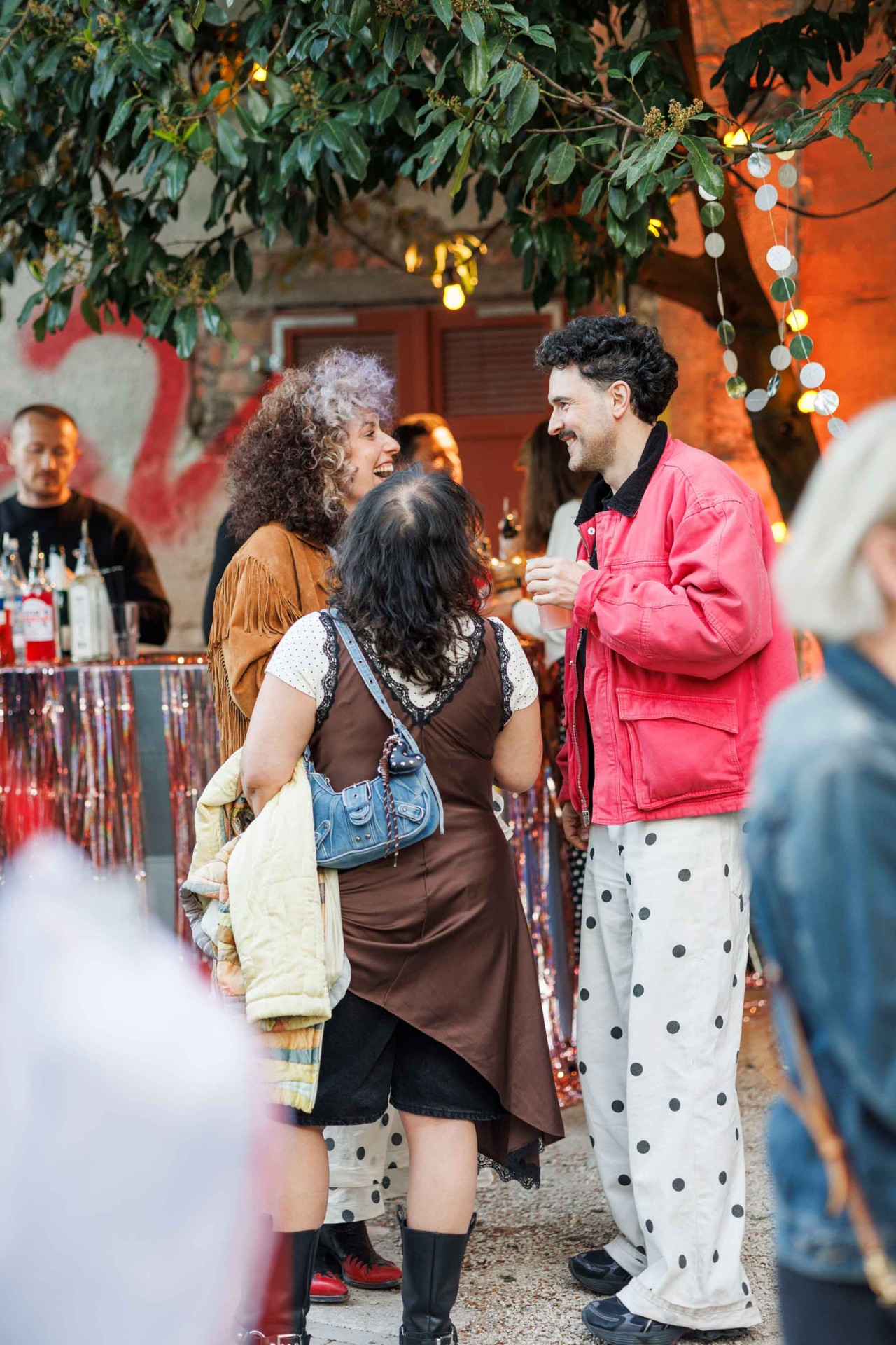 Friends are casually chatting at a festive outdoor setting with lights.
