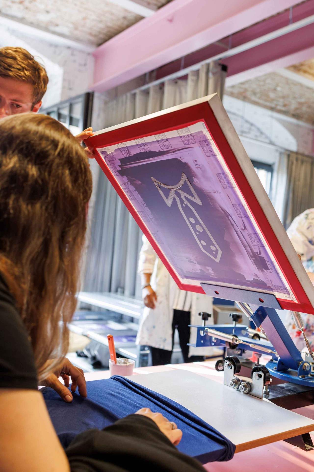 Person screen printing a design on blue fabric in a creative space.