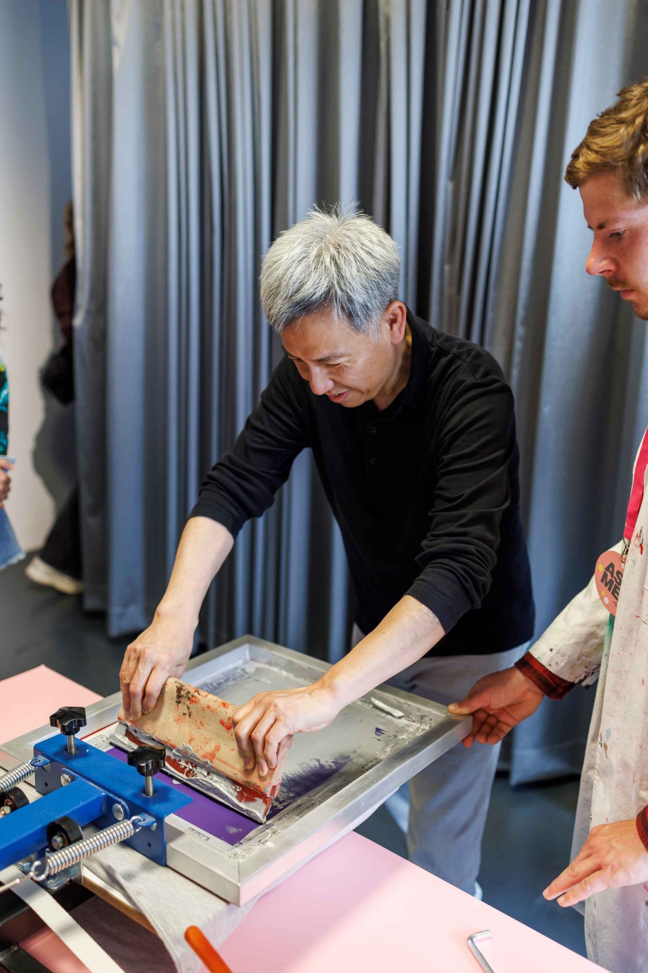 Two people are collaborating on a screen printing machine in a creative studio.