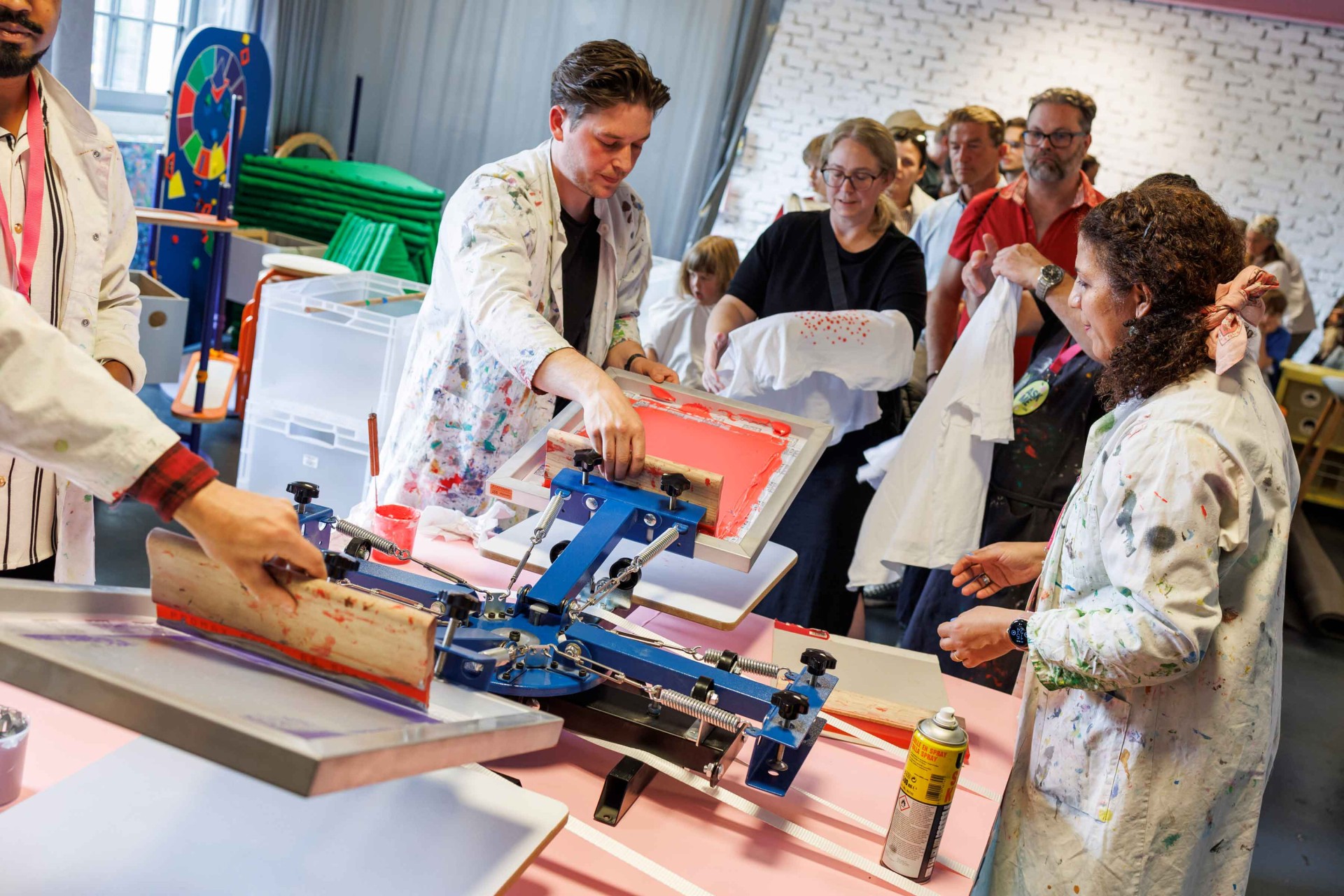 People are working on a screen printing machine to print T-shirts with colorful designs.