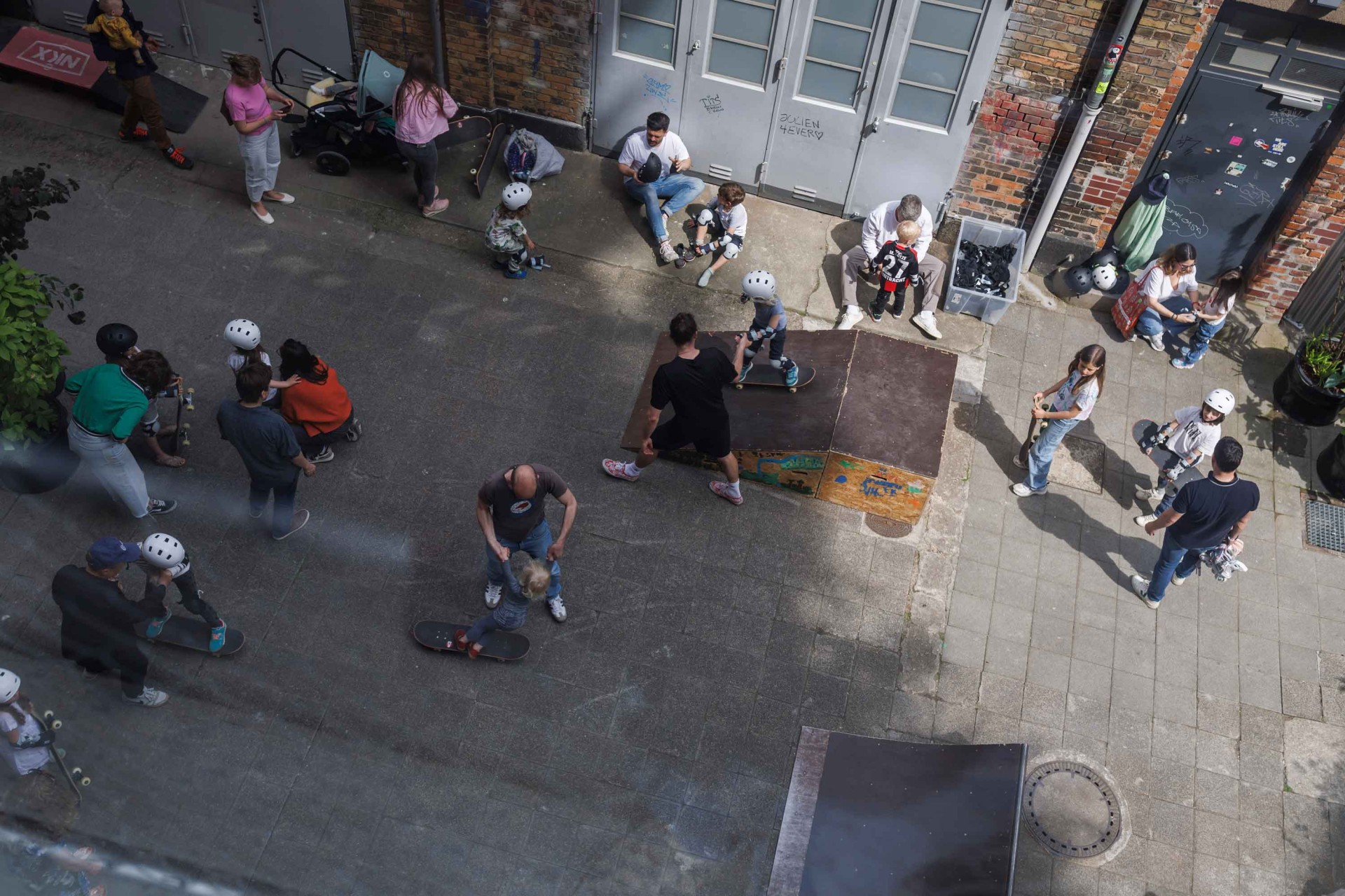 Skaters and kids are trying tricks at a small skatepark in an urban setting. Lots of activity and fun!