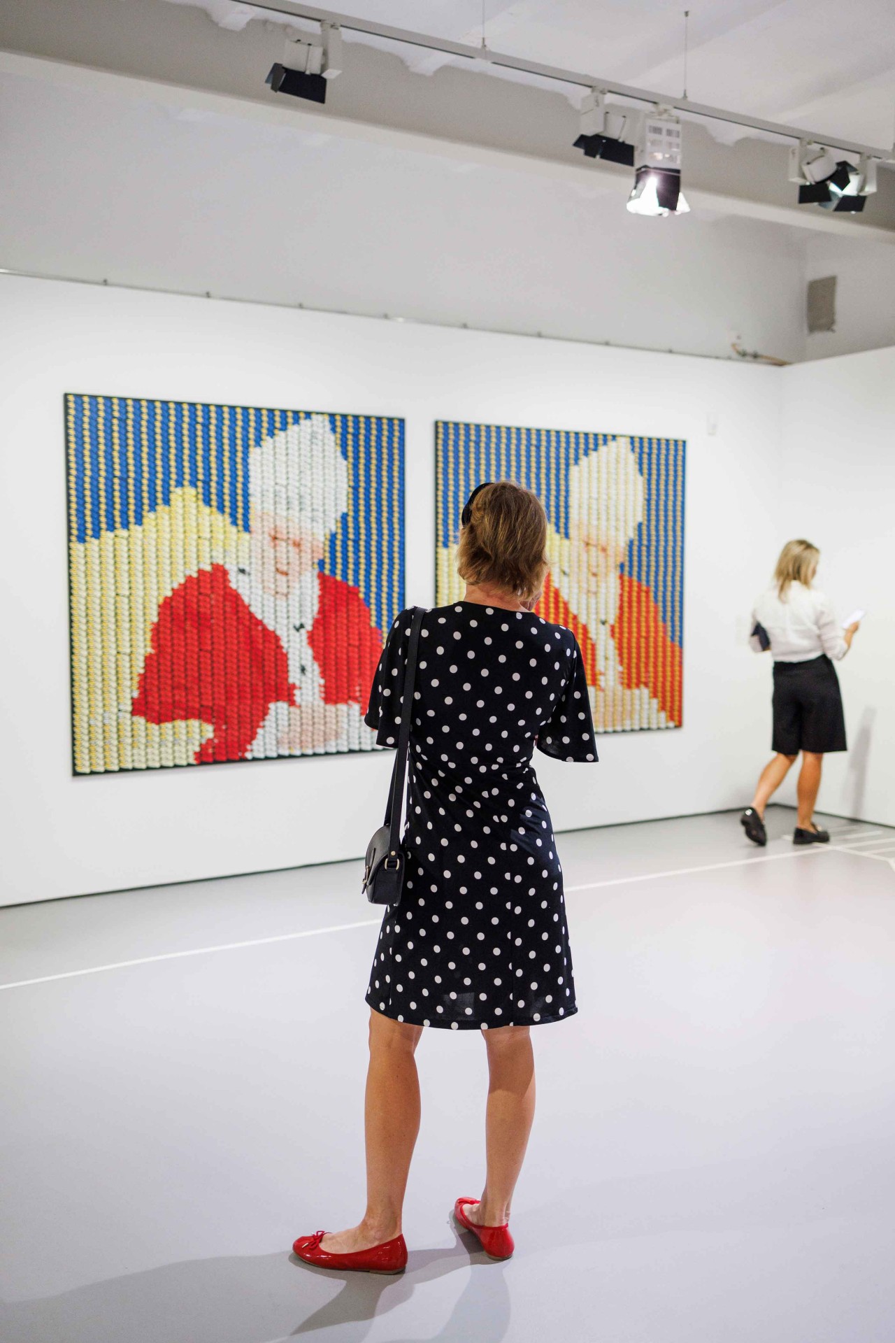 A woman in a polka dot dress looks at modern artworks in a gallery.