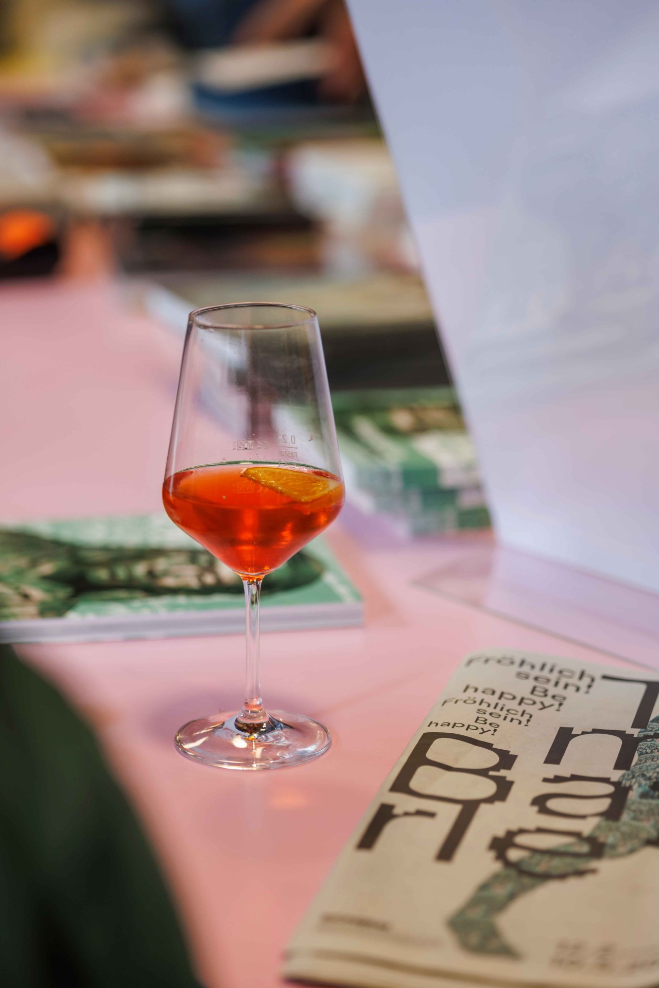 A glass of orange drink with a slice of lemon on a table with magazines.