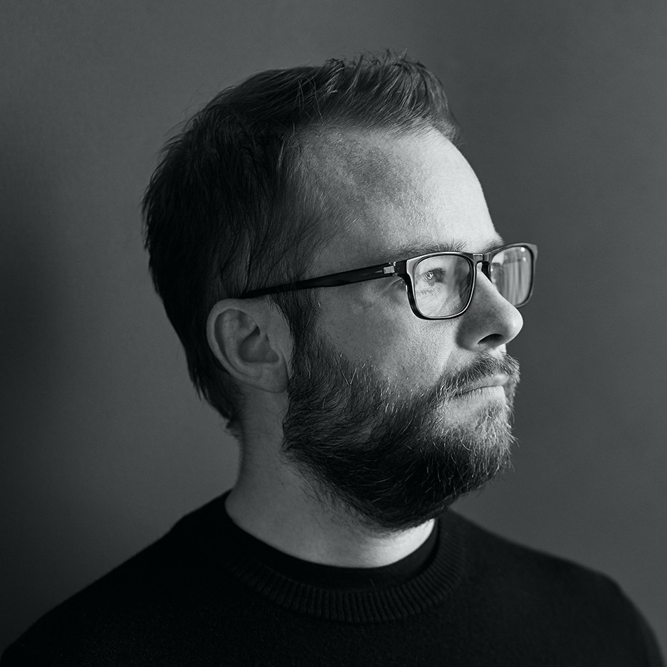 Porträt eines Mannes mit Brille und Bart, in Schwarz-Weiß, seitlich gegen neutralen Hintergrund.