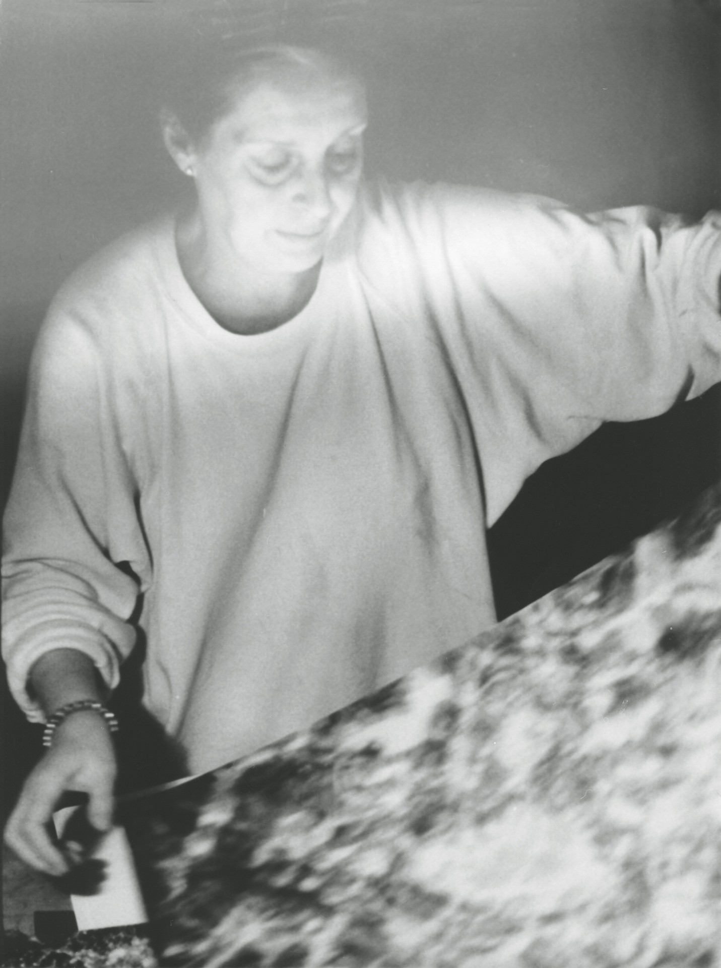 Eine Frau arbeitet konzentriert in einem dunklen Raum an einer großen Textur oder einem Bild.